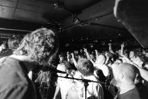 A photo of the band in a packed room in a photo by Sam Sesemann as part of an Idles review