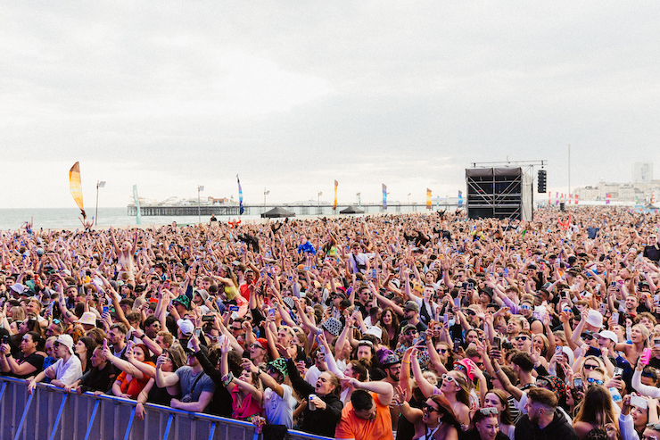 the crowd in the daytime in front of the stage at On The Beach Festival with Brighton Pier in the background