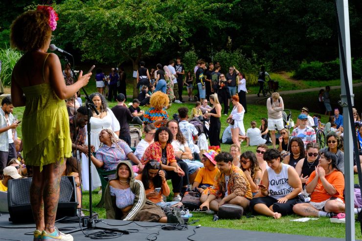 people sitting on the grass listening to a performer on the stage