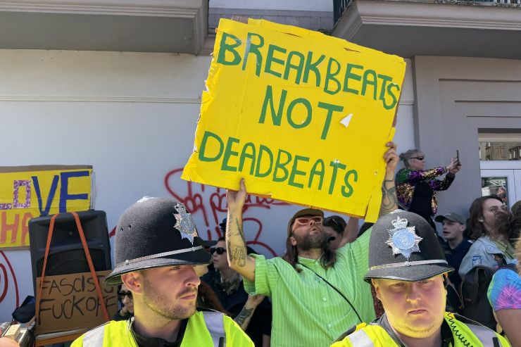 Crowd holding sign that reads 'Breakbeats not deadbeats' behind two police officers